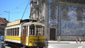 A yellow tram with "CITY TOUR" on the front, parked on a street with a blue and white tiled building in the background.