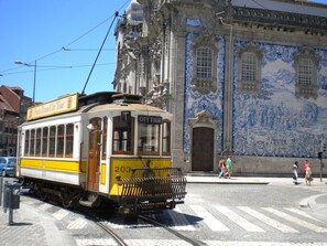 A yellow tram with "CITY TOUR" on the front, parked on a street with a blue and white tiled building in the background. - Porto, City Center Apartment - Right in the Heart of the City! (Porto)