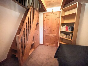 Eine Holztreppe führt zu einer Tür, ein Bücherregal mit Büchern und ein Teppichboden.