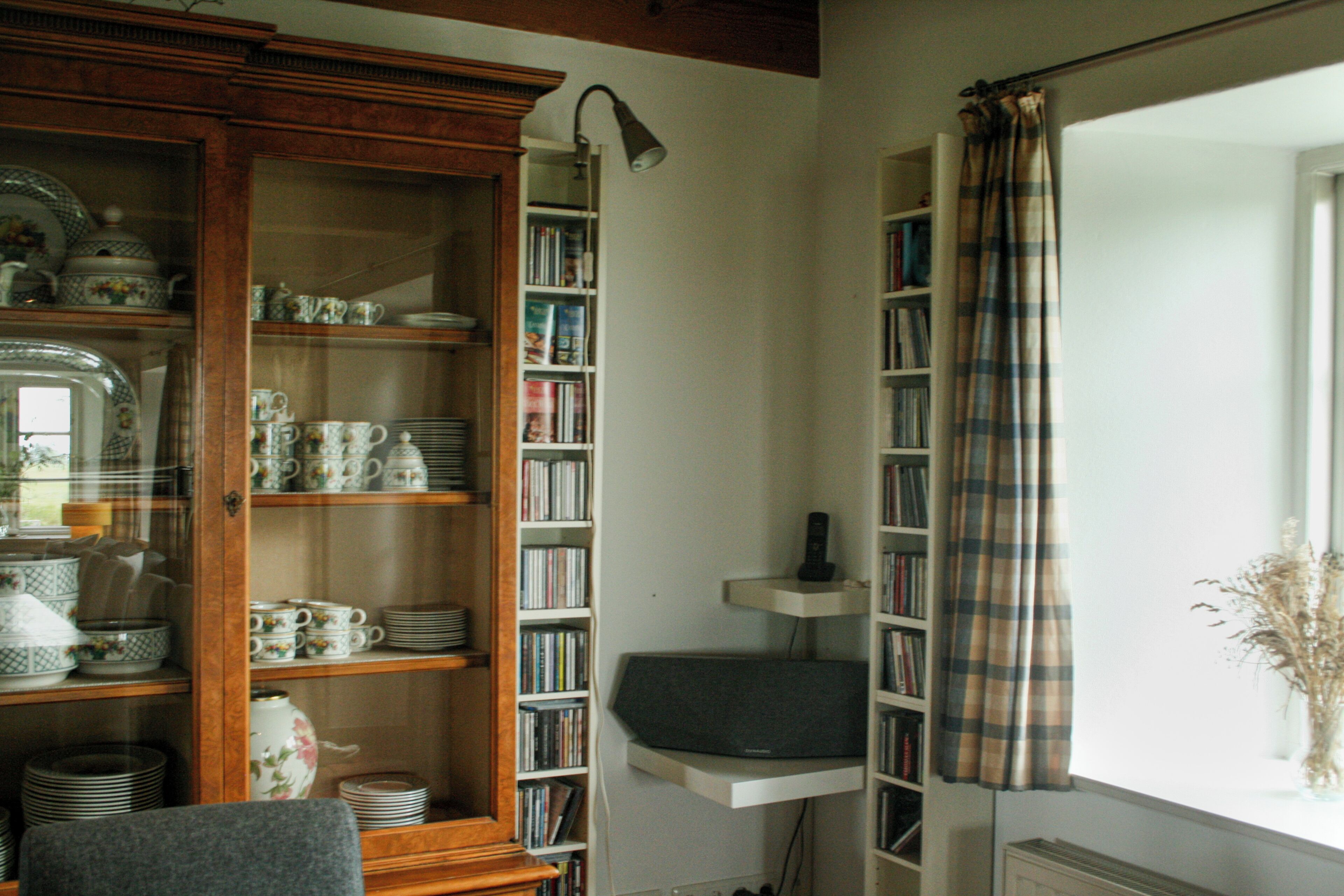 A room with a wooden cabinet containing dishes and a bookshelf filled with books.