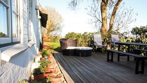 A wooden deck with outdoor furniture, potted plants, and a garden area. - Dream house under thatch with fireplace, sauna, wellness room and lots of space (Poppenbüll)
