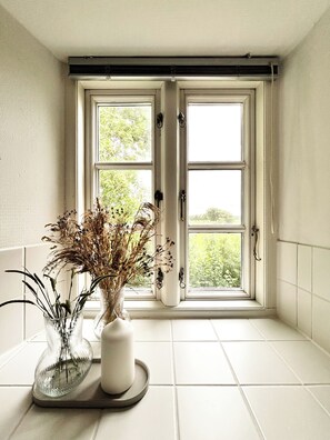 Ein Eckzimmer mit Fenster, einer Topfpflanze und einem gefliesten Boden.