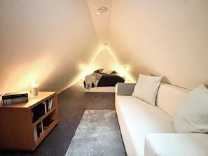 Un dormitorio acogedor en el ático con un sofá blanco, una mesita de noche con lámpara y una estantería.