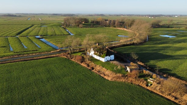 A white house with a green roof surrounded by fields and a small pond. - Dream house under thatch with fireplace, sauna, wellness room and lots of space (Poppenbüll)