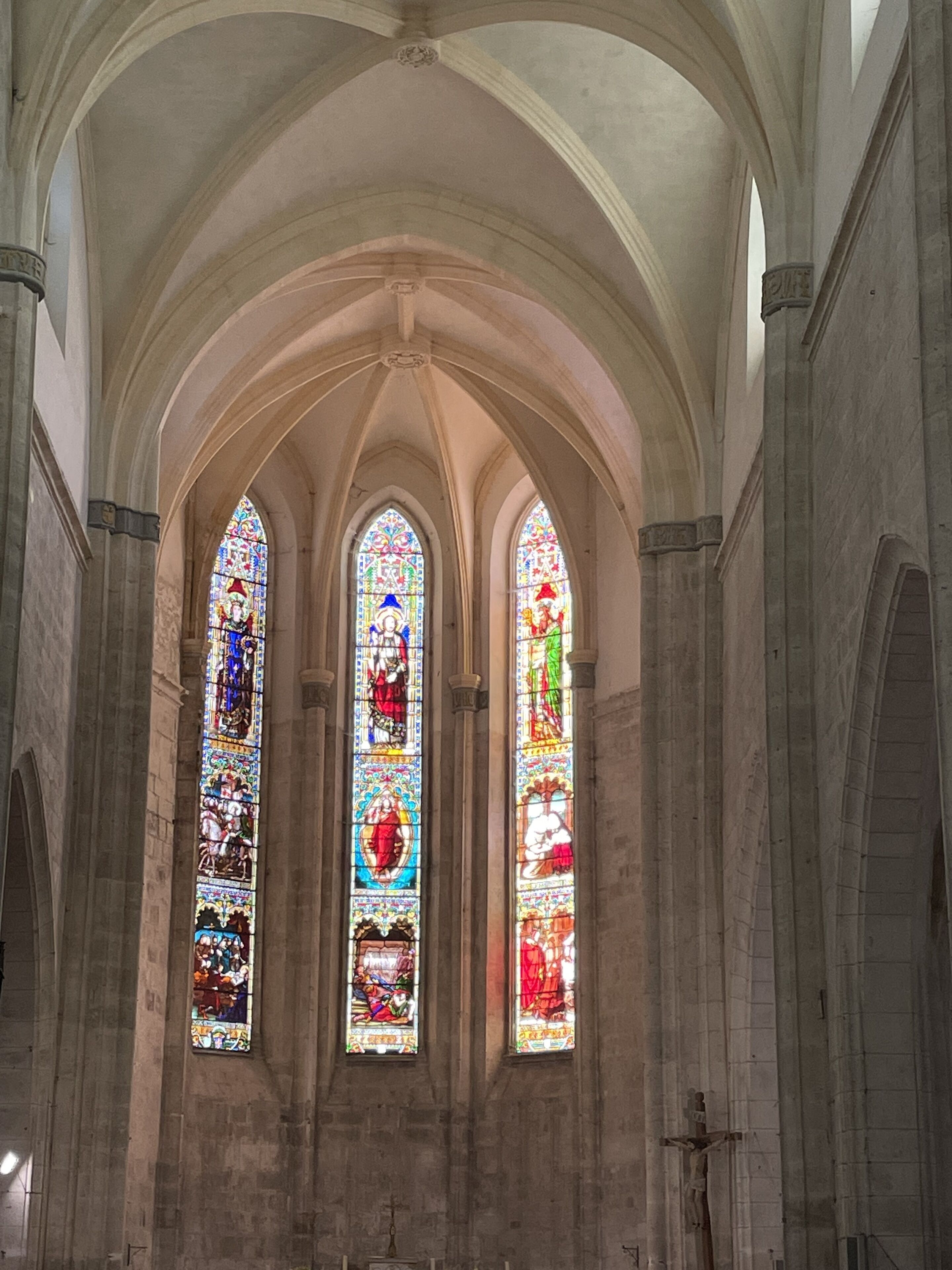 A cathedral interior with three tall stained glass windows and arched ceilings.