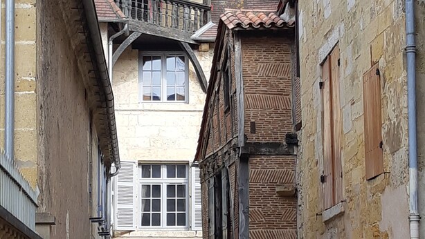A narrow alleyway between buildings with traditional architecture, featuring wooden balconies and stone walls.