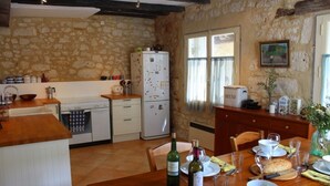 A rustic kitchen with stone walls, wooden countertops, a dining table set with wine glasses, plates, and a loaf of bread.
