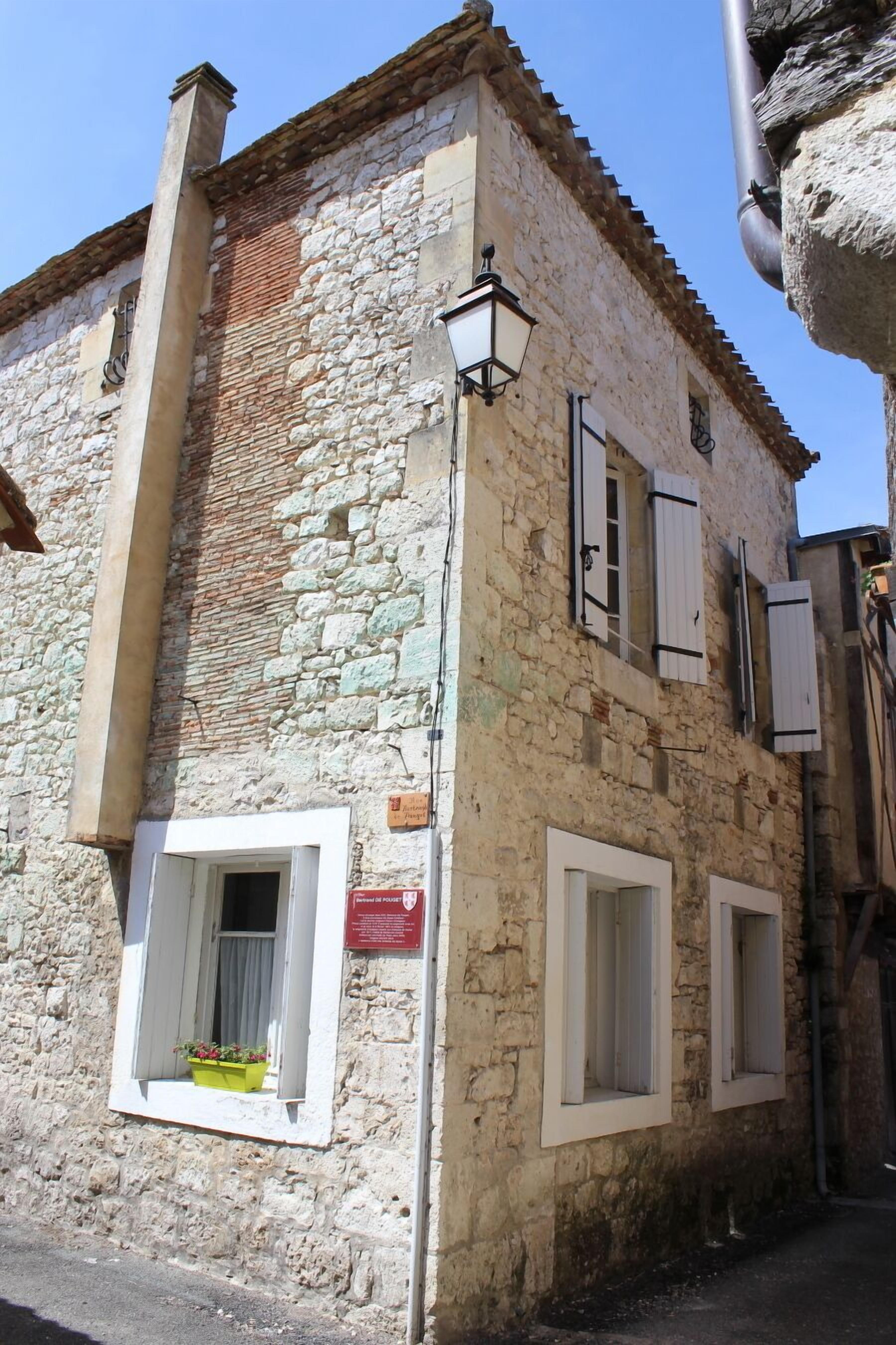Un edificio in pietra con una piccola finestra, una porta, un lampadario e un cartello appeso al muro.