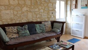 A room with a stone wall, a wooden sofa with patterned cushions, a small table with magazines, and a white cabinet.