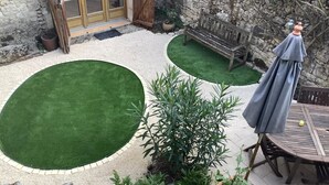 A patio with artificial grass, a wooden bench, a table with chairs, and a covered umbrella.