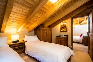 Cozy bedroom with two single beds, wooden nightstand, and dresser, featuring exposed wooden beams.