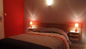 Ein Schlafzimmer mit einem Bett, zwei Nachttischlampen, einer roten Wand und einem hölzernen Kopfteil.