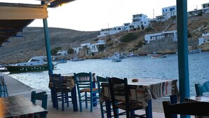 An outdoor seating area with tables and chairs, overlooking a body of water with boats and buildings in the background. - Artemonas: House with character (Artemonas)