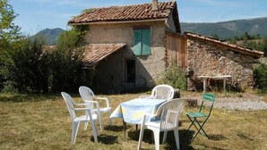 A rustic stone house with a tiled roof, a small porch, and a table with chairs in the foreground. - country holiday home - BARREME (Clumanc)