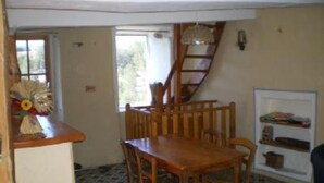 A dining area with a wooden table and chairs, a window with curtains, a staircase, and a small shelf with items. - country holiday home - BARREME (Clumanc)