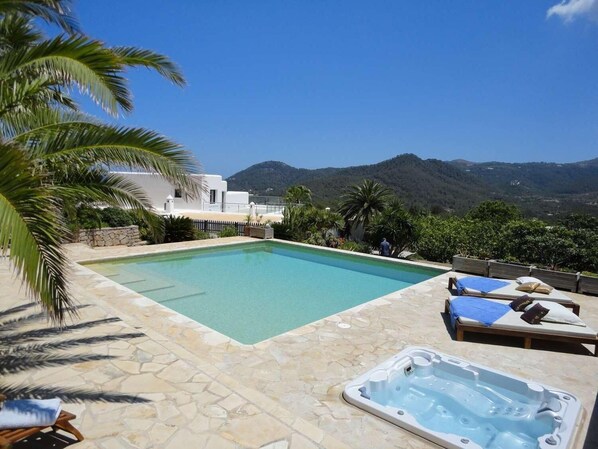 A swimming pool with a hot tub, lounge chairs, and a mountainous backdrop.