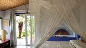 Ein Schlafzimmer mit Bett, Nachttisch, Lampe, einem Gemälde und Blick auf Grünfläche.