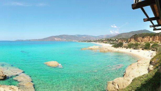 Blick auf die Küste mit klarem türkisblauem Wasser, felsigen Ufern und einer entfernten Bergkette.