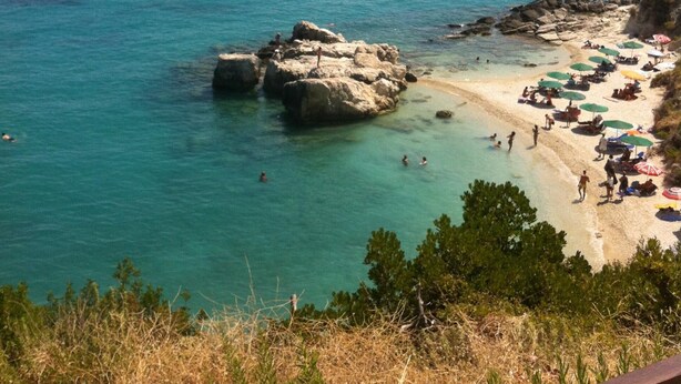 Een strand met helder turquoise water, rotsformaties en een zandstrand.