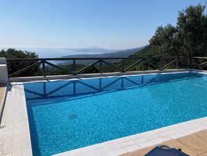 Una piscina blava i nítida amb vista a muntanyes llunyanes, envoltada per una terrassa de fusta i una barana metàl·lica.