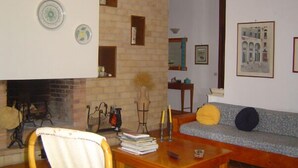 Een woonkamer met een open haard, een bank, een tafel met boeken en een muur met ingelijste foto's.