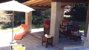 Patio esterno con pavimento in pietra, arredi in legno e struttura a pergola.