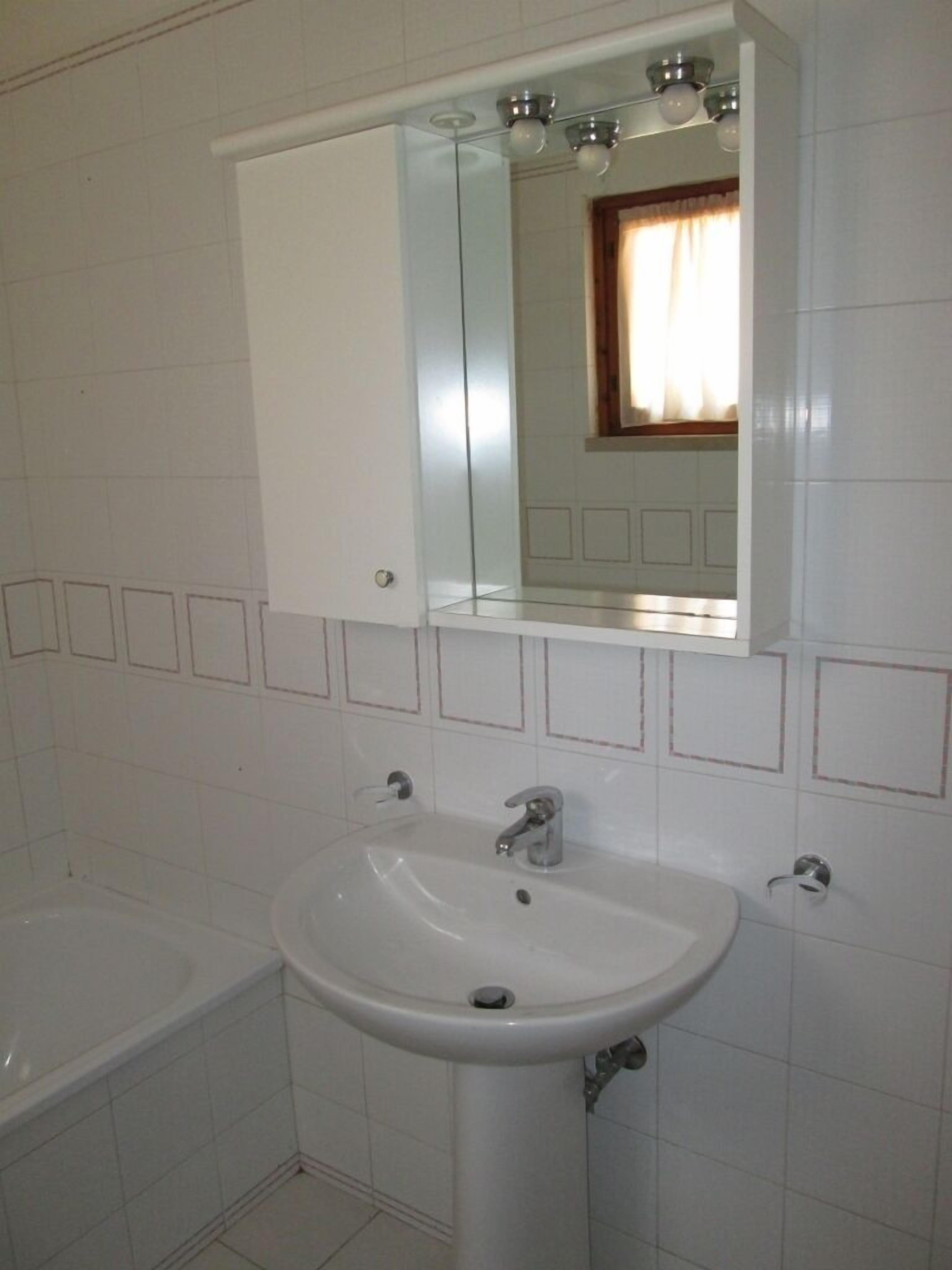A bathroom with a white sink, a mirror above it, and a window with curtains.