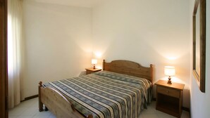 Quarto com cama de madeira, duas mesinhas de cabeceira com abajures e um espelho na parede.