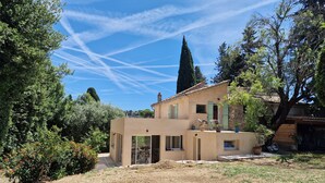 Una casa de dos pisos con un patio, rodeada de árboles y un cielo despejado.