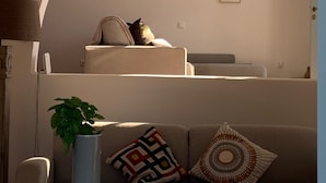 Een woonkamer met een bank, een salontafel met fruit, een vaas met een plant en foto’s in lijsten aan de muur.