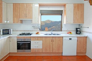 A kitchen with wooden cabinets, a gas stove, a dishwasher, and a window with a mountain view.