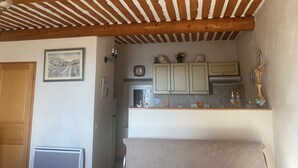 Une cuisine avec des poutres en bois, un tableau représentant un paysage encadré et des placards au-dessus du plan de travail.
