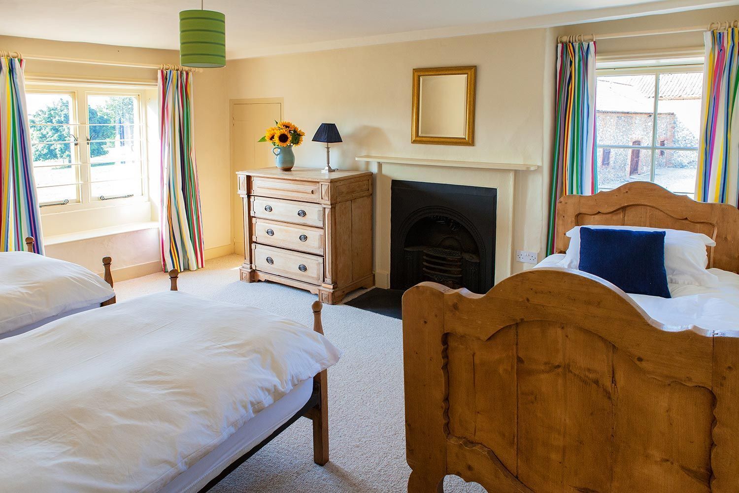 A bedroom with two wooden beds, a dresser, a fireplace, and a window with curtains.