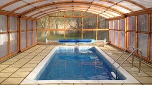 Une piscine intérieure dotée d’un plafond en bois et de murs en verre, entourée d’un sol carrelé.