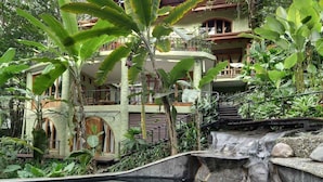A lush tropical resort with a waterfall, a pool, and a multi-story building surrounded by dense vegetation. - 6BR Luxury Ocean View Villa • 3 Private Pools • Chef Included • Sky Deck (Manuel Antonio)