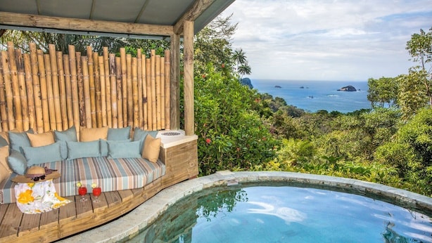 A poolside area with a wooden deck, a cushioned seating area, and a view of the ocean. - 6BR Luxury Ocean View Villa • 3 Private Pools • Chef Included • Sky Deck (Manuel Antonio)
