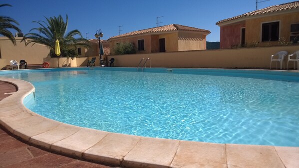 A swimming pool with clear blue water, surrounded by a tiled deck. - Charming and bright apartment in residence with pool and tennis court (Villasimius)