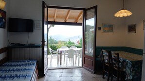 A room with a bed, a desk with a computer, a dining table with chairs, and a view of the outdoors. - Villa Giuliana, Three-room apartment 6/7 Ptl. (Capoliveri)
