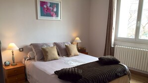 A neatly made bed with a white duvet and decorative pillows, a bedside lamp, and a framed picture on the wall.
