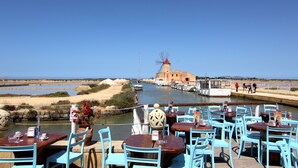 Ein Restaurant am Meer mit Terrassenplätzen, Blick auf einen Hafen und eine Windmühle.