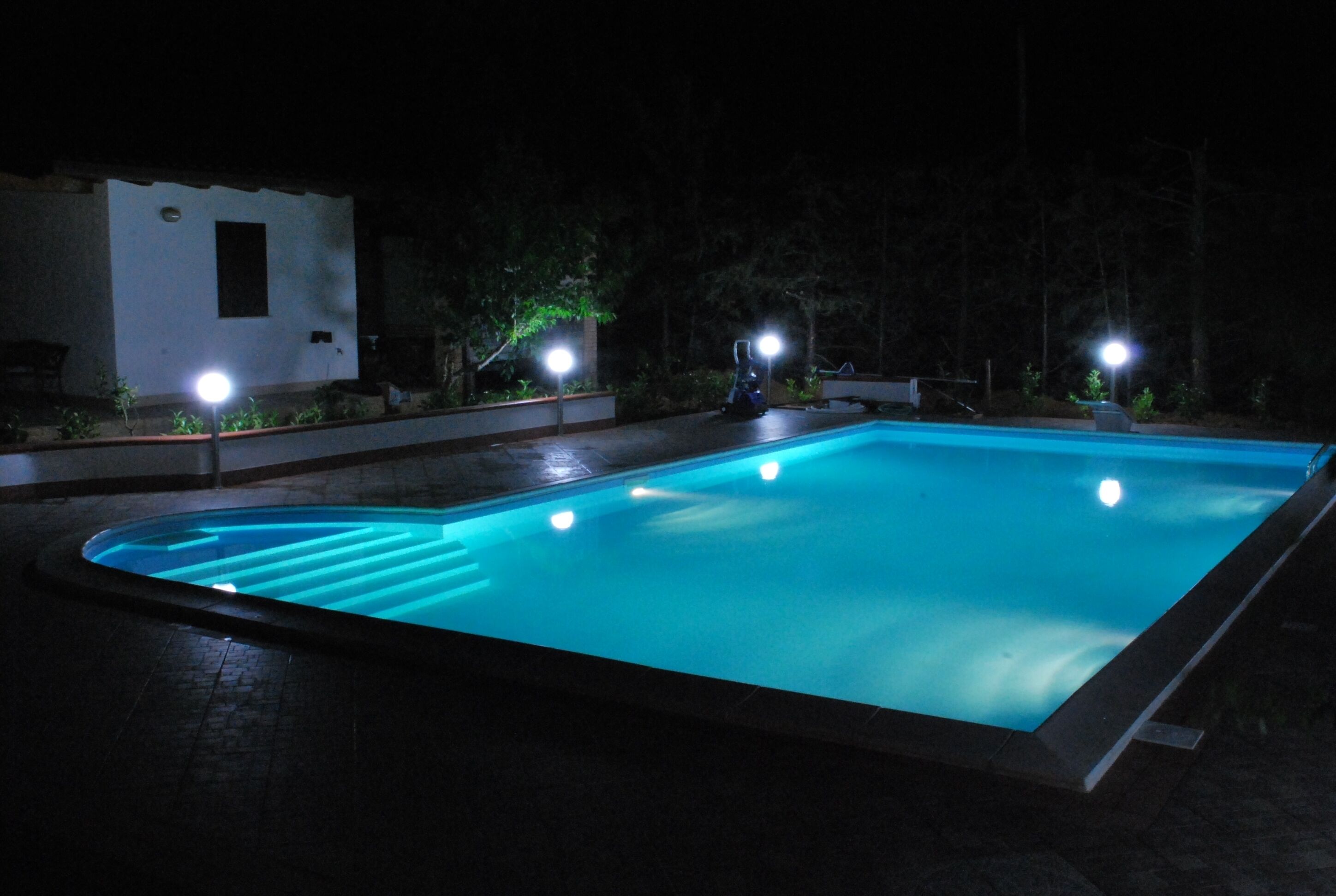 A rectangular swimming pool with a light blue tint, surrounded by a dark patio area.