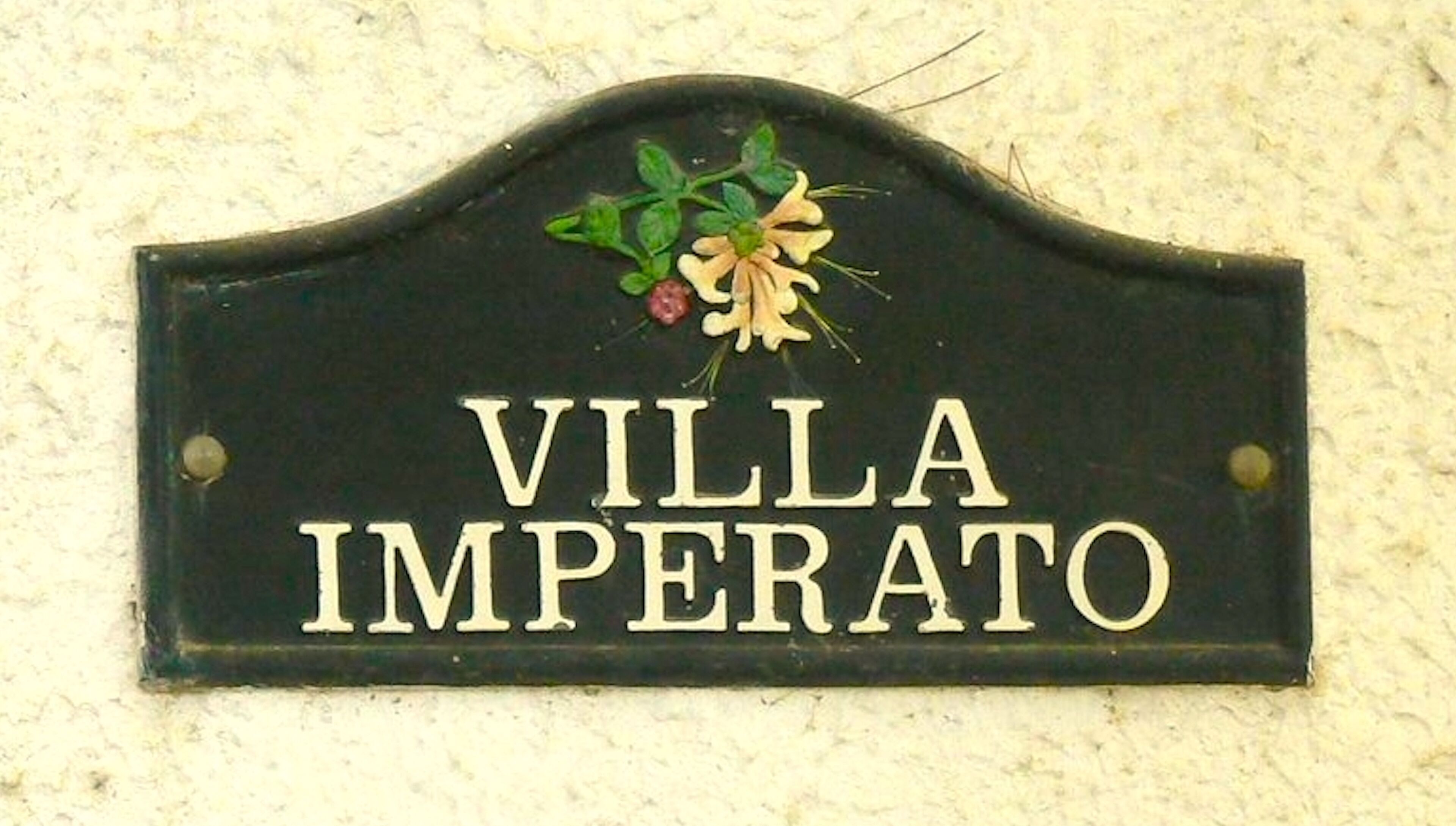 Un letrero negro con las palabras 'VILLA IMPERATO' en letras blancas, sujeto a una pared.
