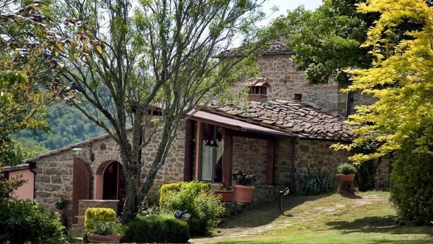 A stone building with a tiled roof, surrounded by a well-maintained garden and trees. - Independent villa in the panoramic countryside (Greve In Chianti)