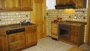 A kitchen with wooden cabinets, a dishwasher, an oven, and a tiled backsplash. - Nice apartment at ground level in Ruhpolding, children and pets are welcome (Bayern)