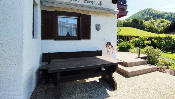 A building named "Haus Berggub" with a wooden bench outside, a window with brown shutters, and a stone plaque. - Nice apartment at ground level in Ruhpolding, children and pets are welcome (Bayern)