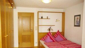 A bedroom with a wooden bed, a door, and a shelf with decorative items. - Nice apartment at ground level in Ruhpolding, children and pets are welcome (Bayern)