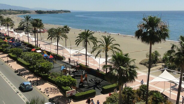 Ein Strand mit Palmen, einem Spielplatz und Blick aufs Meer.