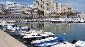 Ein Yachthafen mit verschiedenen dort liegenden Booten, eine Uferpromenade und mehrstöckige Gebäude im Hintergrund.