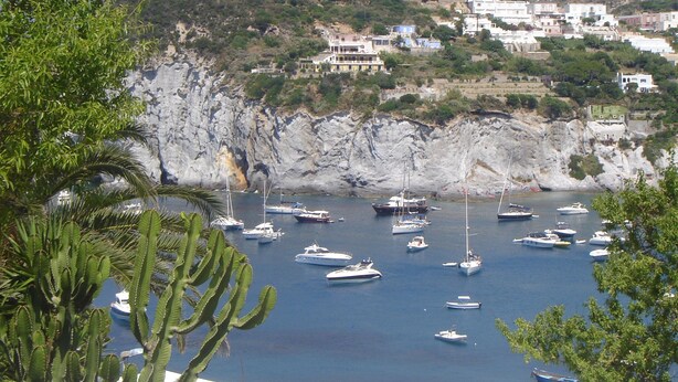 A coastal town with numerous boats docked in a marina, surrounded by rocky cliffs and lush greenery. - The house by the sea one step away from the beach (ponza)