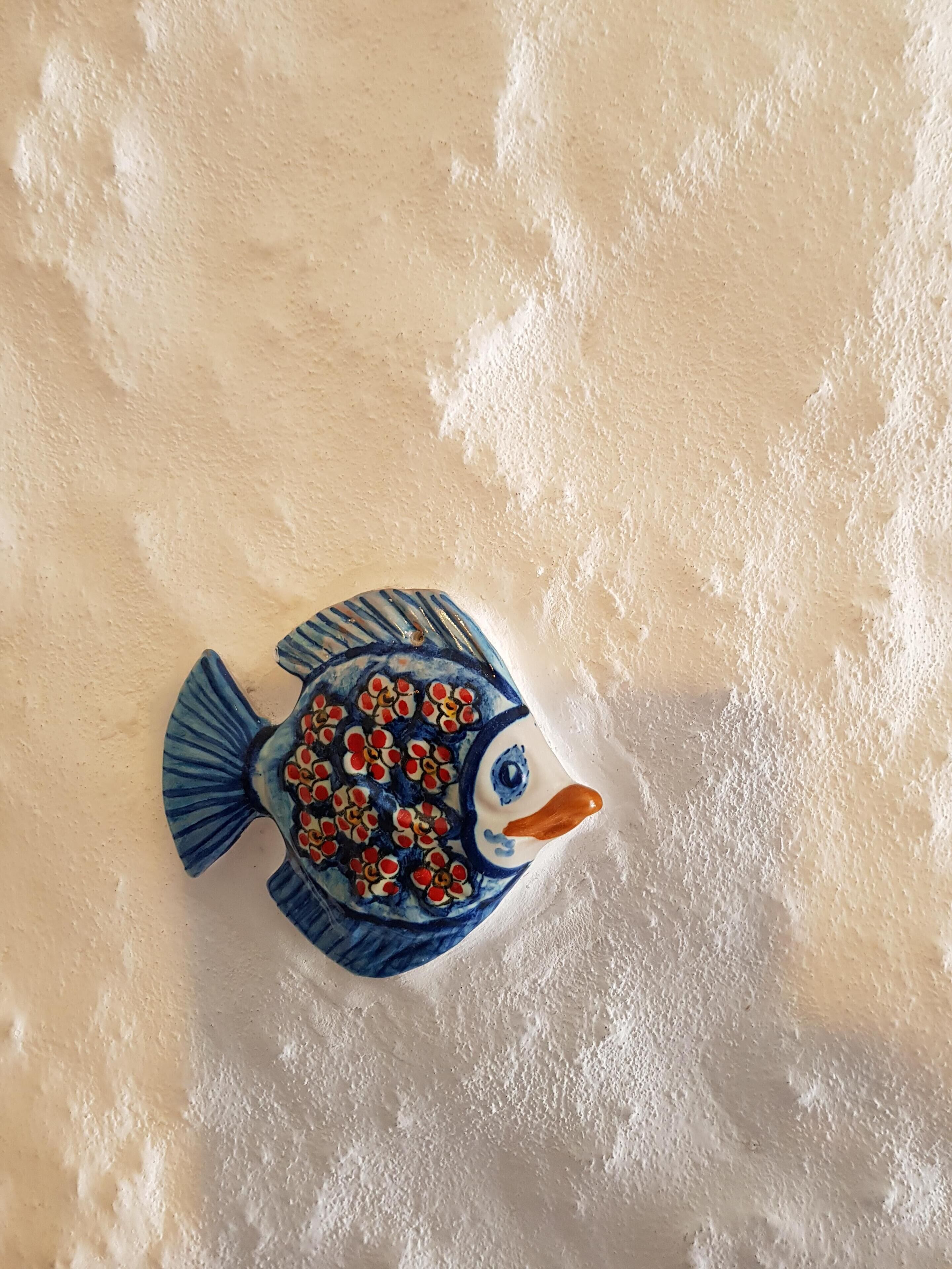 A ceramic fish decoration on a textured wall.